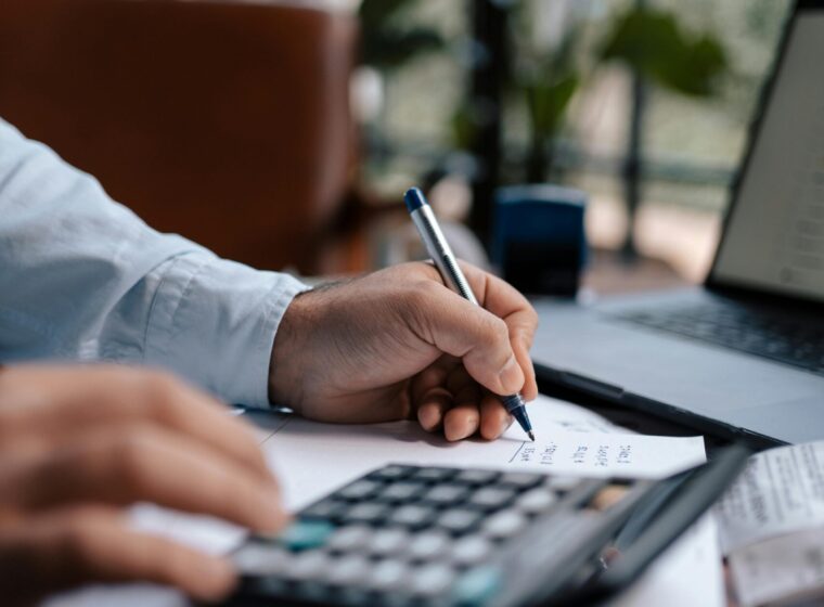 Free A person calculating finances with a calculator and pen on a desk indoors. Stock Photo