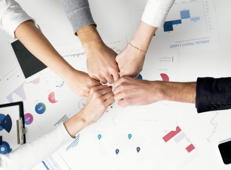 Free Colleagues celebrate success with a fist bump over financial charts depicting teamwork and unity. Stock Photo