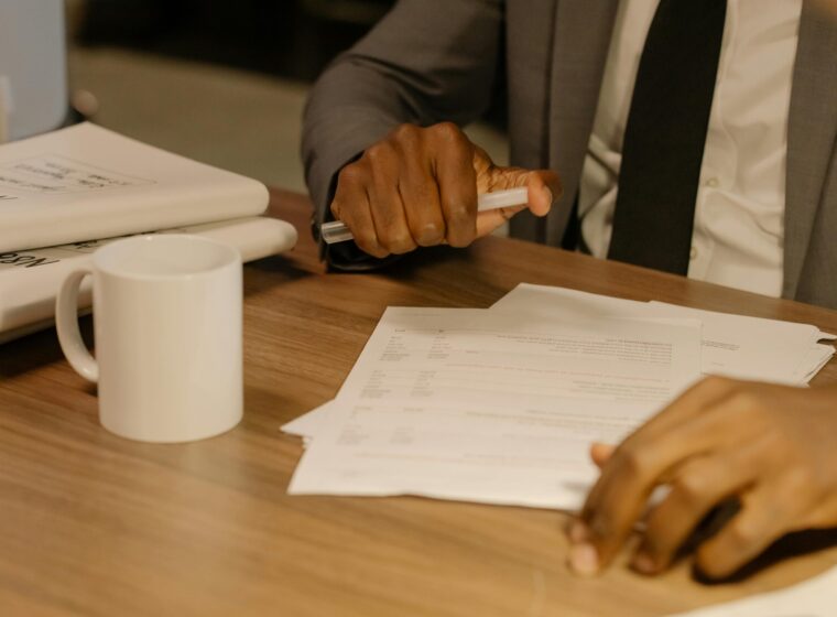 Free Close-up of a businessman holding and reviewing documents on a wooden desk. Stock Photo