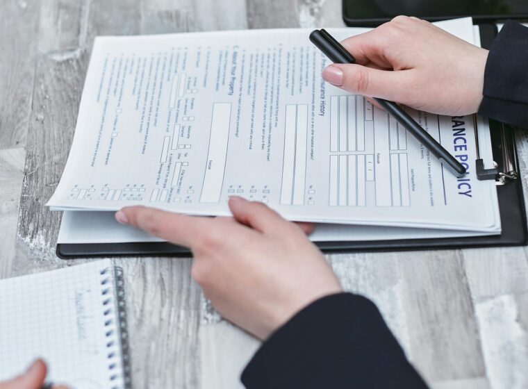 Free Close-up of hands analyzing insurance policy paperwork with pen on table. Stock Photo